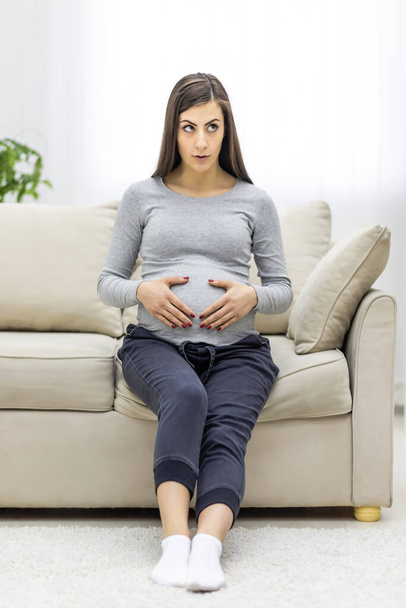 Photo of pregnant woman looking at camera and touching her stomach. Concept of pregnant woman. - Photo, image