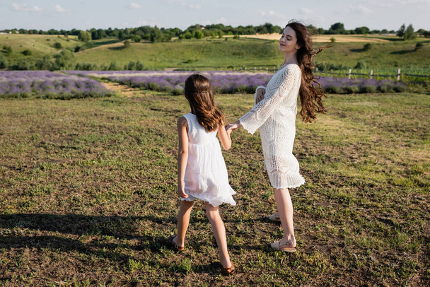 happy pregnant woman holding hands with daughter while walking in field - Photo, Image