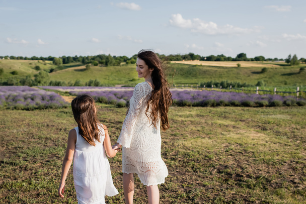 smiling pregnant woman in openwork dress walking with daughter in countryside - Foto, imagen
