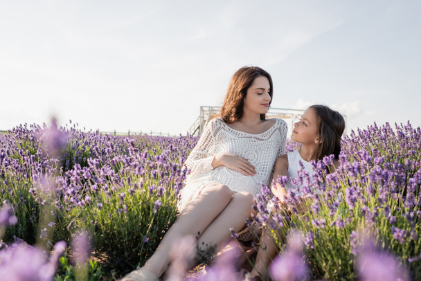 cheerful girl and pregnant woman looking at each other in lavender field - 写真・画像