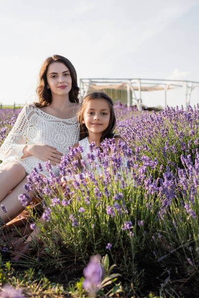 happy girl with pregnant mother looking at camera in lavender meadow - Fotó, kép