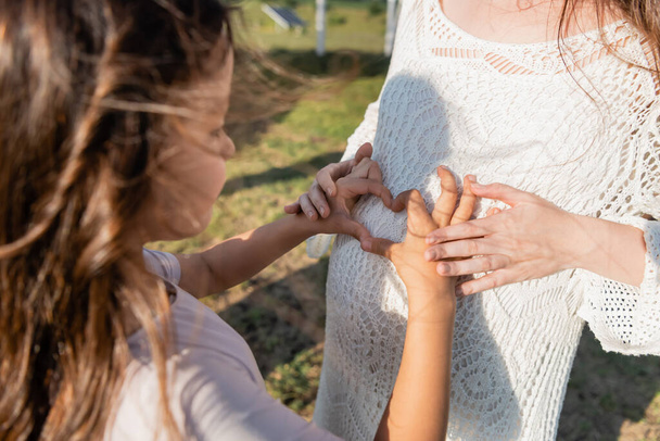 blurred girl showing heart sign near belly of pregnant mother - Fotografie, Obrázek