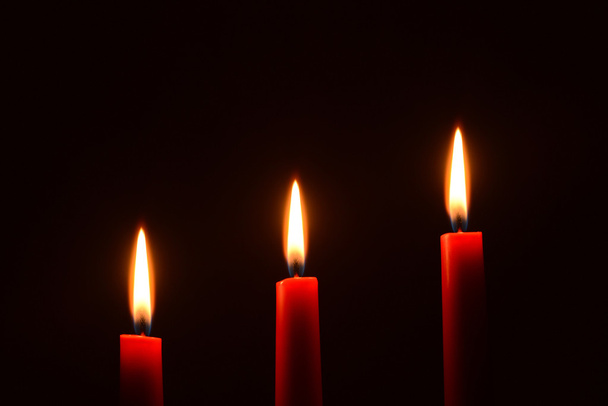 Kolme punaista kynttilää mustalla taustalla
 - Valokuva, kuva