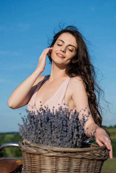 pretty brunette woman with long hair smiling near blurred lavender flowers - Foto, Imagen