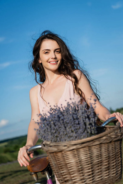 cheerful woman with long hair looking at camera near blurred lavender - Fotoğraf, Görsel
