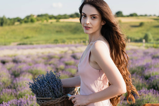 long haired woman with lavender flowers looking at camera outdoors - Foto, Imagen