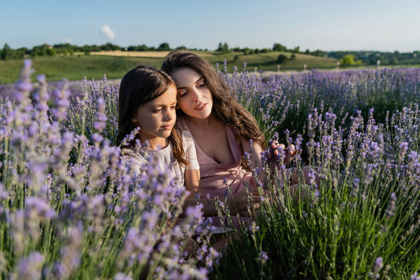 brunette woman and girl sitting in lavender field on summer day - Foto, Bild