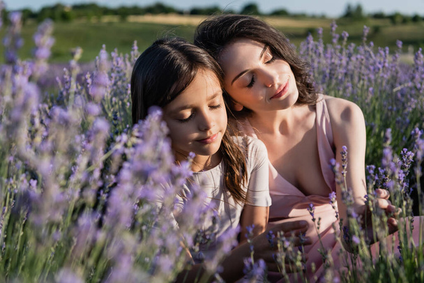 pleased mom and daughter with closed eyes in meadow with flowering lavender - Foto, Imagen