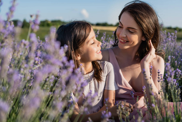 happy mom and daughter smiling at each other in blurred lavender field - Photo, image