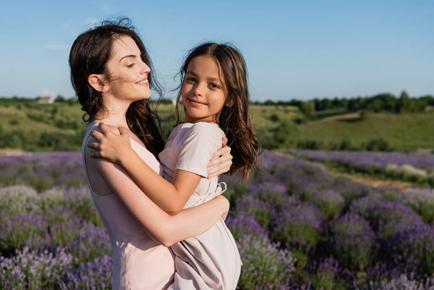 brunette woman embracing daughter smiling at camera in lavender meadow - Foto, Imagem