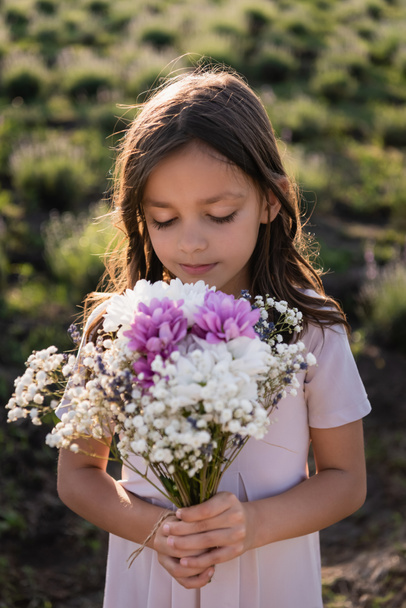 girl with long hair holding bouquet of flowers in meadow - Fotoğraf, Görsel