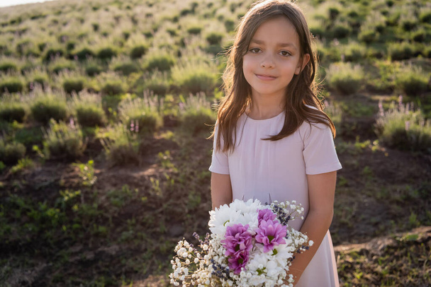 brunette girl with bouquet looking at camera in green field - Photo, Image