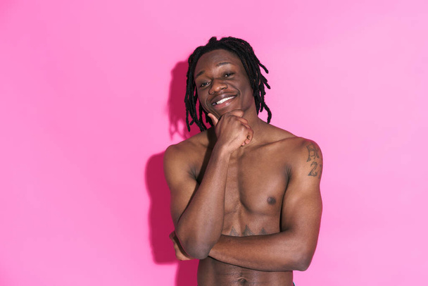 Black shirtless man with dreadlocks smiling and looking at camera isolated over pink background - Foto, immagini