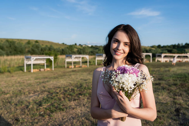pleased woman with flowers smiling at camera on farmland - Foto, Imagem