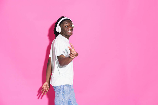 Young black man listening music with headphones and gesturing isolated over pink background - Фото, изображение