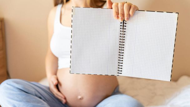 Pregnant woman writing list. Young pregnancy mother holding notepad. Pregnant lady writing check list of baby. Concept maternity, childbirth - Photo, Image