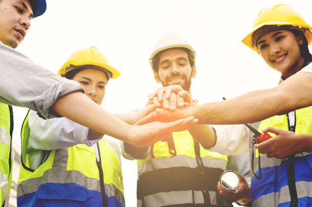 Group of contractors, engineers and formats in safety vests with helmets join hands to work together to successfully complete a construction project on construction site. cooperation and success concept - Foto, Imagen