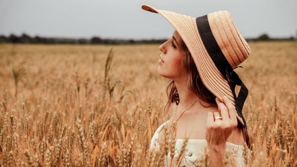 女小麦畑の自然。日没の夏の小麦畑で太陽の帽子の幸せな若い女性。コピースペース、日没、フレアライト、夏の季節。ボホシックなスタイル - 写真・画像