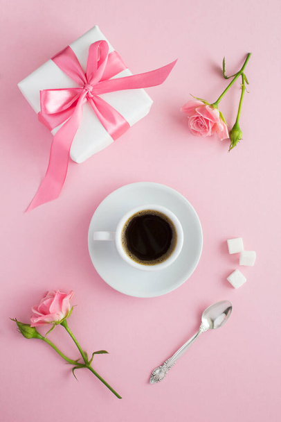 Black coffee in the white cup, pink roses and gift box on the pink  background. Top view. Location vertical. - Photo, Image