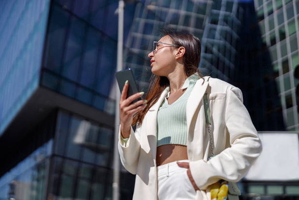 Attractive young woman in white suit near business centre. City walking concept - Fotó, kép