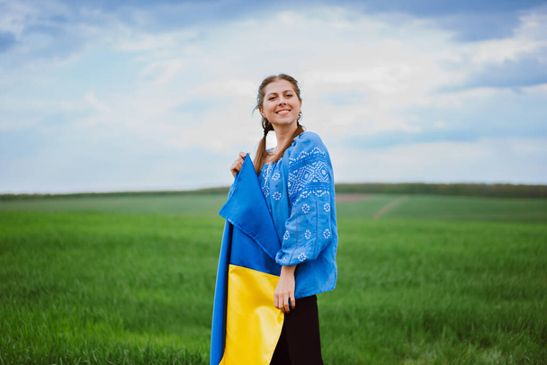 Beautiful ukrainian woman with national flag on green field background. Young lady in blue embroidery vyshyvanka. Ukraine, independence, freedom, patriot symbol, victory in war. High quality photo - Foto, Imagen