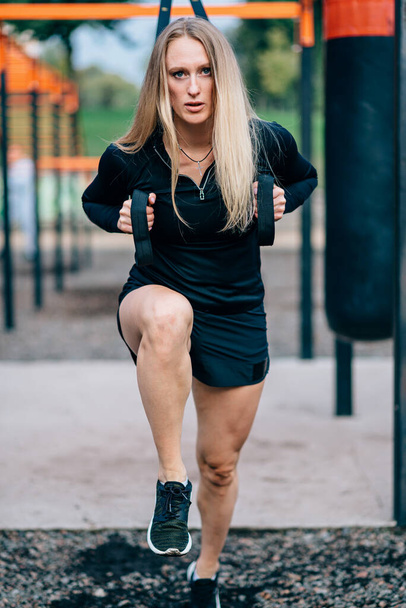 Woman in workout. Young athletic female in sportswear trains with fitness straps on sports ground. - Zdjęcie, obraz