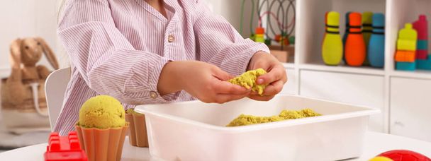 Cute little girl playing with bright kinetic sand at table in room, closeup. Banner design - Photo, Image