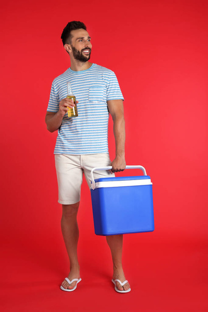 Happy man with cool box and bottle of beer on red background - Foto, imagen