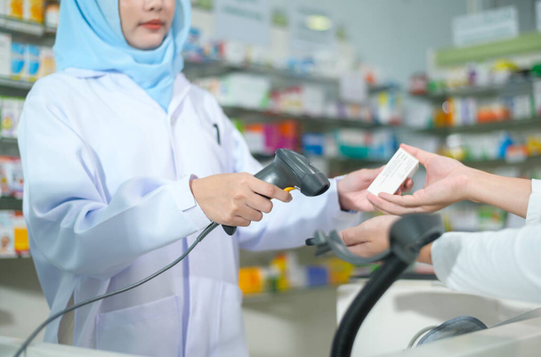 A Female muslim pharmacist scanning barcode in a modern pharmacy drugstore. - Фото, изображение