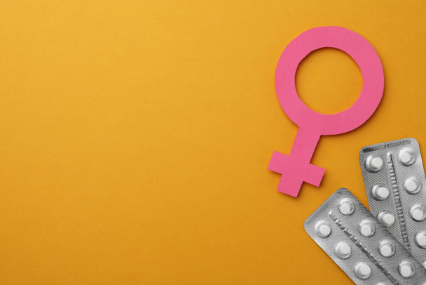 Female gender sign, blisters of pills and space for text on orange background, flat lay. Women's health concept - Foto, afbeelding