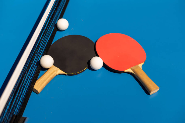 Ракетки для настольного тенниса и белый пластиковый мяч на синем фоне
 - Фото, изображение