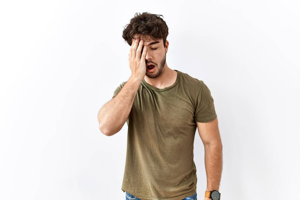 Hispanic man standing over isolated white background yawning tired covering half face, eye and mouth with hand. face hurts in pain.  - Foto, Imagen