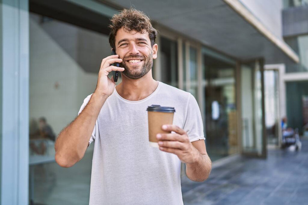 Fiatal spanyol férfi beszél az okostelefonon kávézás az utcán - Fotó, kép