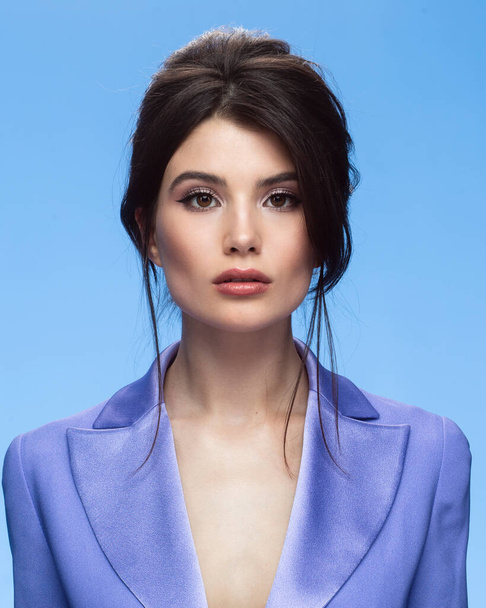 Front image of a sexy brunette in a stylish purple suit in attractive, looking at camera, isolated blue background. - Foto, immagini