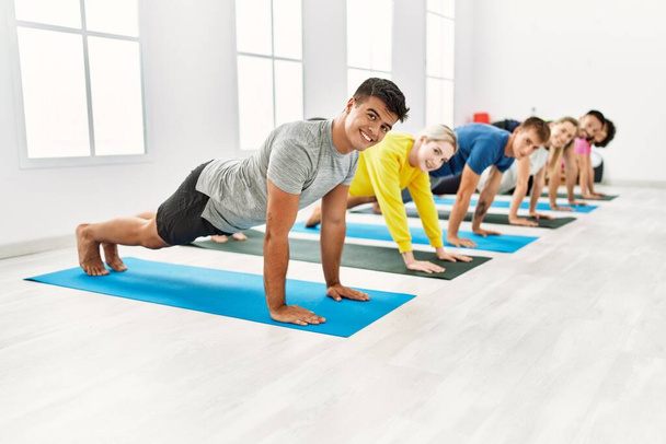 Grupo de jóvenes sonriendo feliz entrenamiento yoga en el centro deportivo. - Foto, Imagen