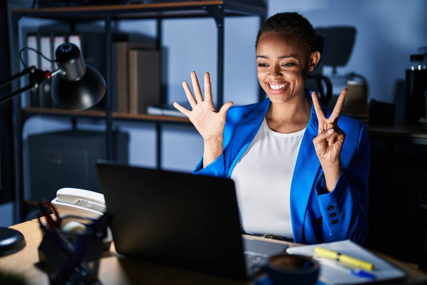 Mulher americana africana bonita trabalhando no escritório à noite mostrando e apontando para cima com os dedos número sete, sorrindo confiante e feliz.  - Foto, Imagem