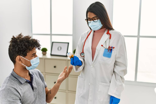 Fiatal latin orvos nő ad üveg tablettát a férfi orvosi szobában. - Fotó, kép