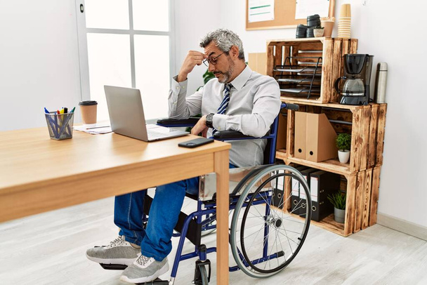 Middelbare leeftijd Spaanse man werkt op kantoor zitten op rolstoel moe wrijven neus en ogen gevoel vermoeidheid en hoofdpijn. stress en frustratie concept.  - Foto, afbeelding