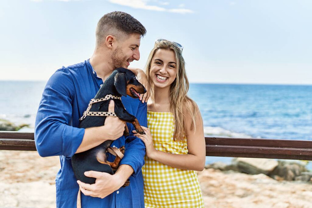 Jeune couple caucasien souriant heureux et câlin avec chien à la plage. - Photo, image
