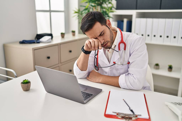Young hispanic man wearing doctor uniform stressed working at clinic - Fotoğraf, Görsel