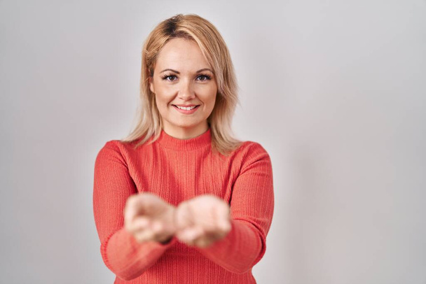 Blonde woman standing over isolated background smiling with hands palms together receiving or giving gesture. hold and protection  - Foto, imagen