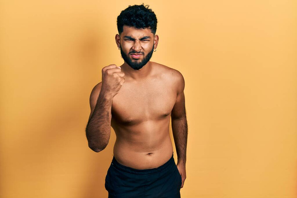 Arab man with beard wearing swimwear shirtless angry and mad raising fist frustrated and furious while shouting with anger. rage and aggressive concept.  - Foto, afbeelding