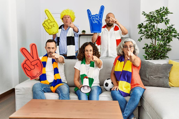 Ομάδα ηλικιωμένων που υποστηρίζουν την ποδοσφαιρική ομάδα στο σπίτι δείχνοντας με το δάχτυλο την κάμερα και σε σας, με αυτοπεποίθηση χειρονομία που φαίνεται σοβαρή  - Φωτογραφία, εικόνα