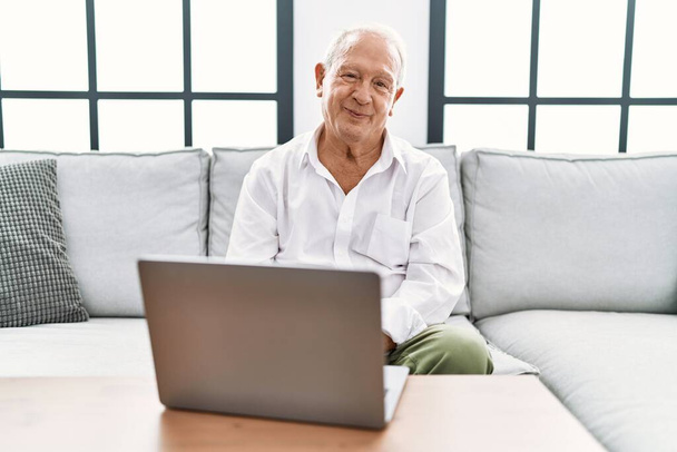 Старший чоловік використовує ноутбук вдома, сидячи на дивані, розслаблений серйозним виразом обличчя. простий і природний погляд на камеру
.  - Фото, зображення