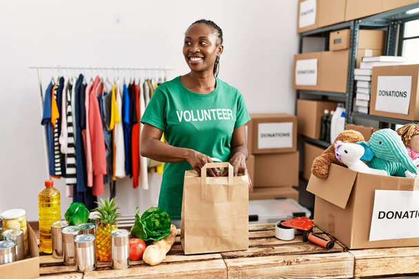 Mladý africký americký dobrovolník žena příprava papírové tašky s jídlem v charitativním centru. - Fotografie, Obrázek