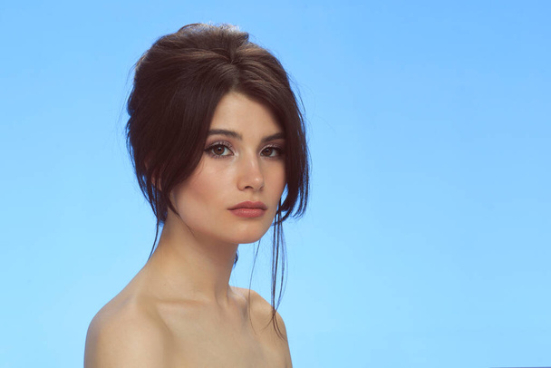 Beauty portrait of a brunette with bare shoulders with makeup and hairstyle, isolated blue background. - Foto, imagen