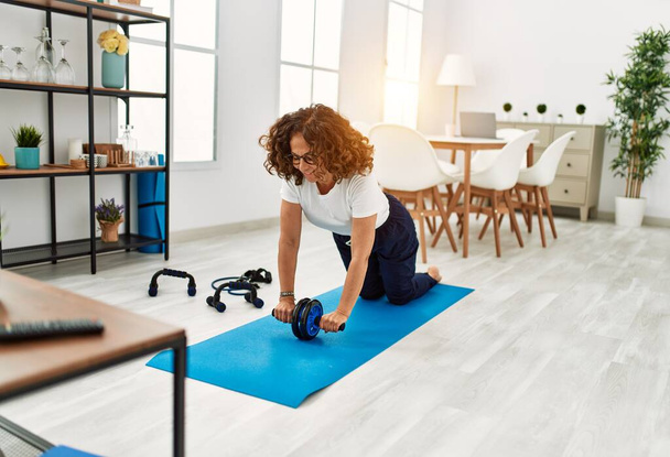 Mature hispanic woman doing exercise with abdominal wheel at the living room at home - Foto, Bild