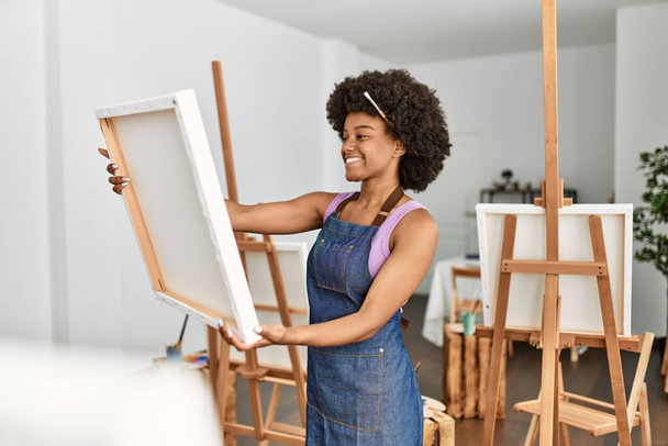 Joven mujer afroamericana sonriendo confiada sosteniendo dibujo de lona en el estudio de arte - Foto, imagen