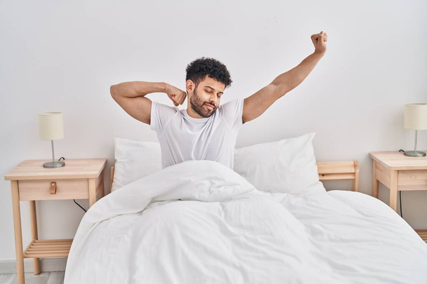 Young arab man waking up stretching arms at bedroom - Fotoğraf, Görsel