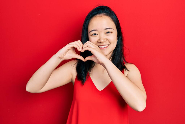 Young chinese girl wearing casual clothes smiling in love doing heart symbol shape with hands. romantic concept.  - Φωτογραφία, εικόνα